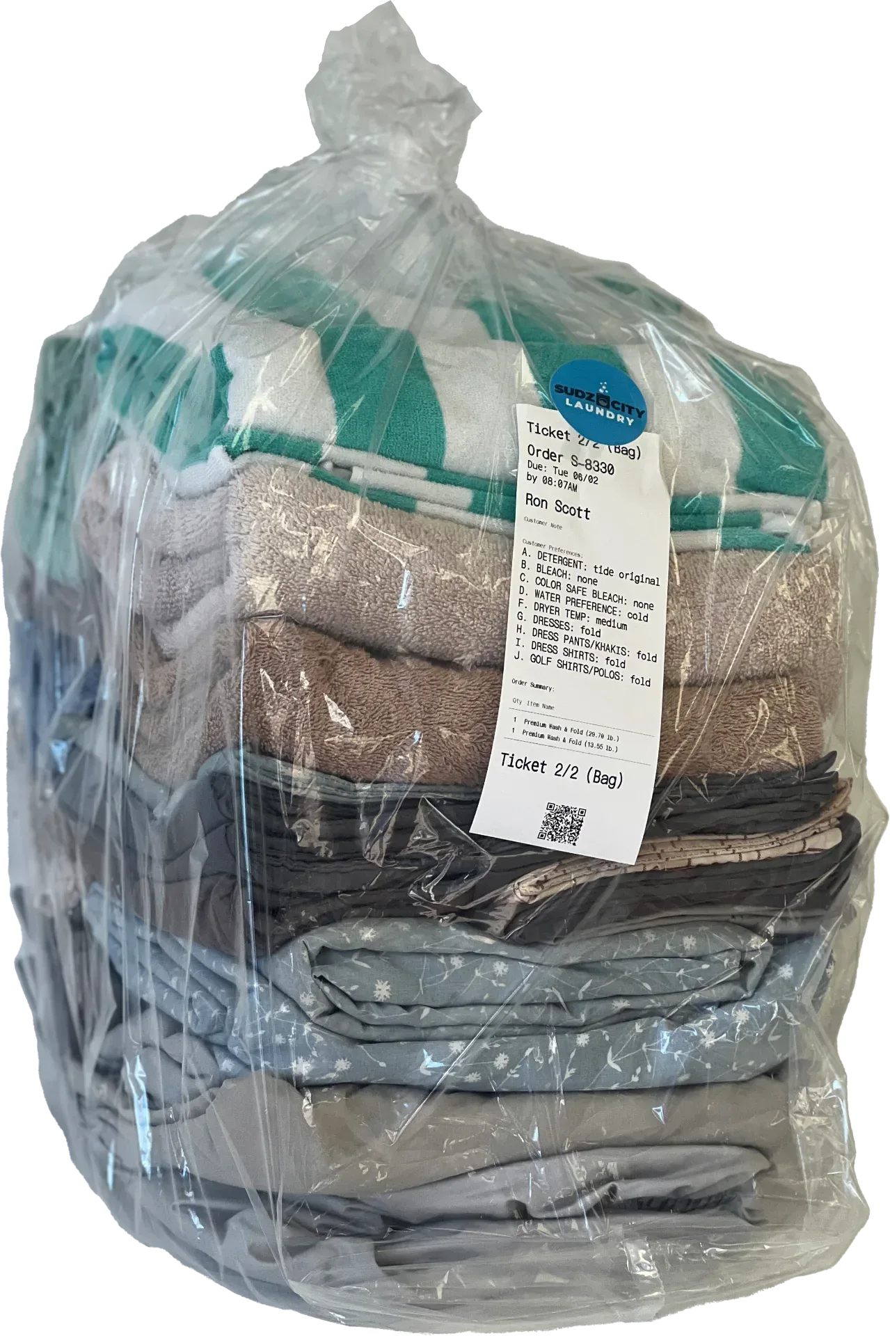 Folded laundry returned in a clear protective Sudz City bag with order ticket